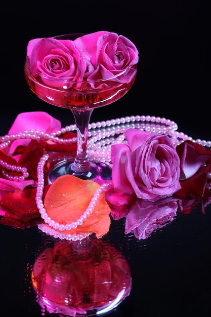 Composition avec du vin mousseux rose et des roses en verre, isolées sur fond noir