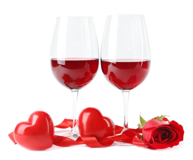 Composition avec du vin rouge dans des verres, rose rouge, ruban et coeurs décoratifs isolés sur blanc