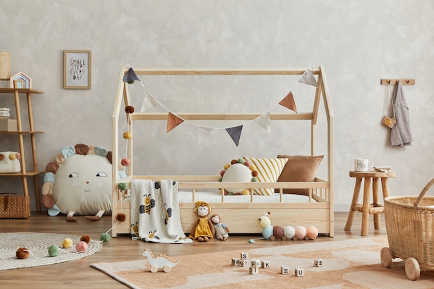 Composition élégante de l'intérieur de la chambre d'enfant scandinave confortable avec lit en bois et table basse, jouets en peluche et en bois et décorations suspendues en textile. Mur créatif, tapis au sol. Modèle.