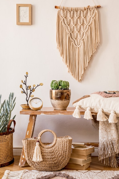 Photo composition élégante de l'intérieur du salon avec cadre, banc en bois, oreiller, plaid, sac pour femme, livres, cactus, macramé, plante, décoration et accessoires personnels élégants dans un décor moderne.