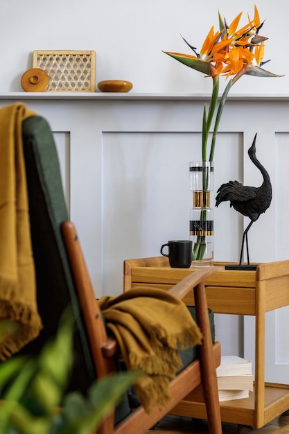 Composition élégante à l'intérieur du salon avec fauteuil design, plaid, plante, tasse de café, fleur dans un vase, livre, panneaux de bois avec étagère et accessoires presonal élégants dans un décor moderne.