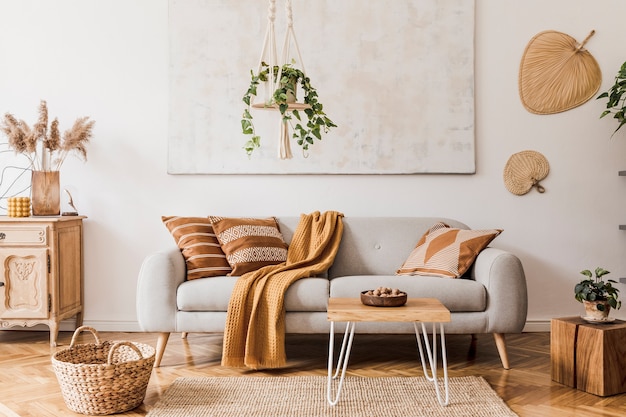 Composition élégante d'un intérieur de salon créatif et confortable avec canapé gris, table basse, plantes, tapis et beaux accessoires. Murs blancs et parquet au sol.