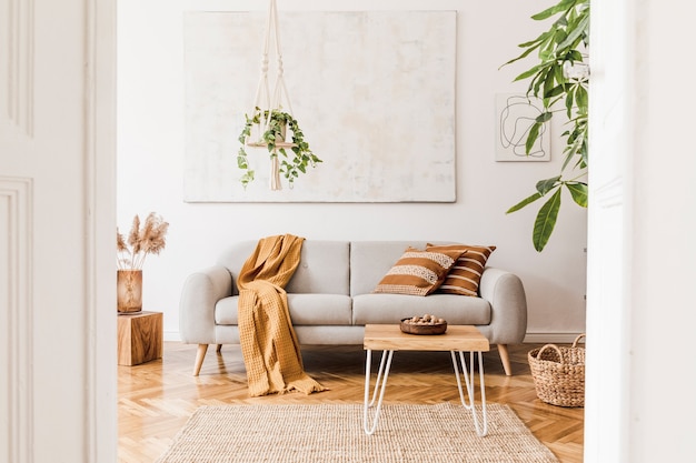 Composition élégante d'un intérieur de salon créatif et confortable avec canapé gris, table basse, plantes, tapis et beaux accessoires. Murs blancs et parquet au sol.