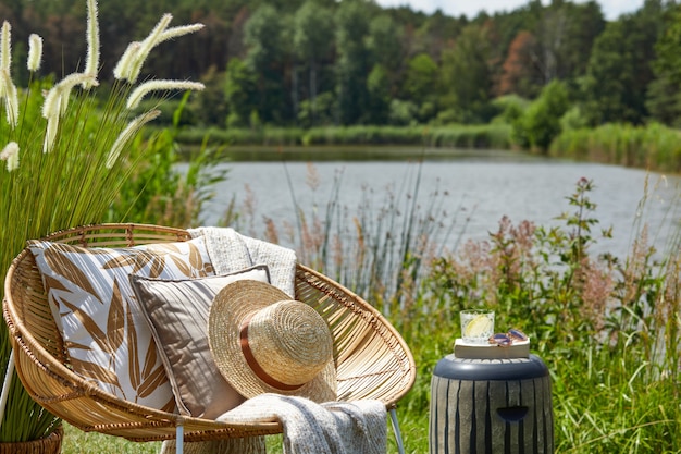 Composition élégante de jardin extérieur sur le lac avec fauteuil en rotin design table basse oreillers à carreaux boissons et accessoires élégants