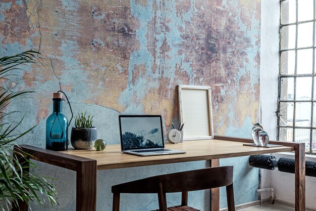 Photo composition élégante et moderne de l'intérieur de l'espace de travail créatif avec table et chaise en bois, plante et accessoires. cette chambre spacieuse présente des murs créatifs et du parquet.