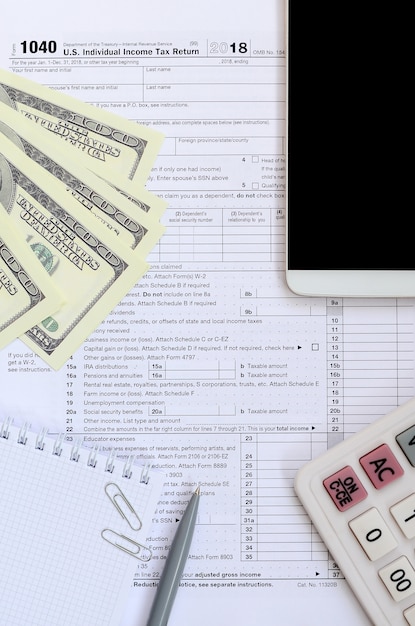 Composition des éléments figurant sur le formulaire d’impôt 1040. Billets d&#39;un dollar, stylo, calculatrice, smartphone, trombone et bloc-notes