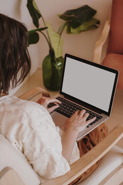 Composition esthétique avec une jeune jolie femme travaillant sur un ordinateur portable avec un écran d'espace de copie assis sur une chaise Design d'intérieur moderne