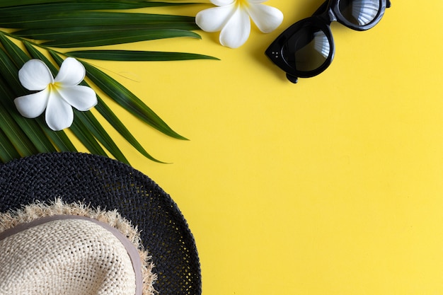 Composition d'été avec chapeau, lunettes de soleil, feuille de palmier tropical et fleurs sur fond jaune