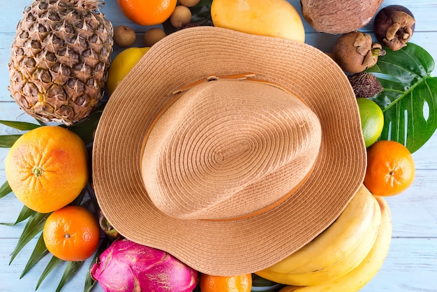 Composition D'été. Feuilles De Palmier Tropical, Chapeau, Beaucoup De Fruits Sur Un Fond En Bois Bleu.