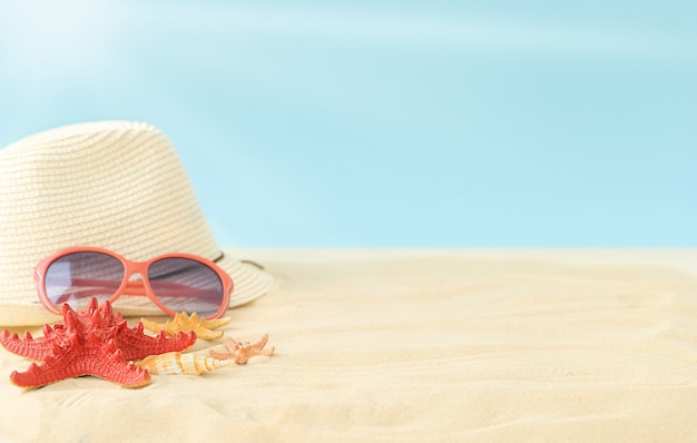 Composition d'été de la plage ensoleillée avec des lunettes de soleil chapeau ciel soleil et étoiles de mer sur le sable