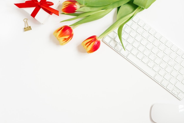 Composition féminine de l'espace de travail des femmes, cadeaux. Cadeau avec un ruban rouge et un bouquet de fleurs de tulipes, clavier. Vue à plat et vue de dessus