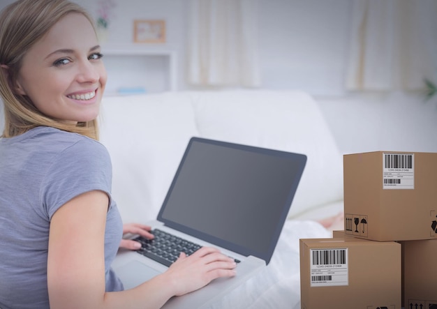 Photo composition d'une femme souriante utilisant un ordinateur portable dans une nouvelle maison avec une pile de boîtes en carton. déménagement, expédition mondiale et concept de livraison image générée numériquement.