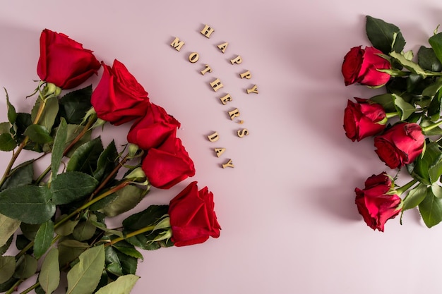 Une composition festive de roses rouges sur fond rose avec l'inscription en lettres en bois bonne fête des mères vue de dessus style plat