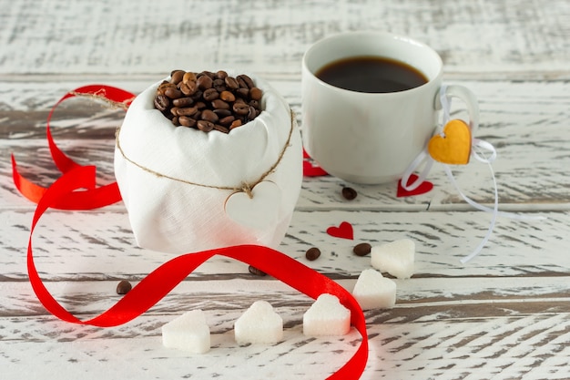 Composition festive de la Saint-Valentin. Café romantique noir avec du sucre en forme de coeur et des confettis de coeur en papier rouge dispersé.