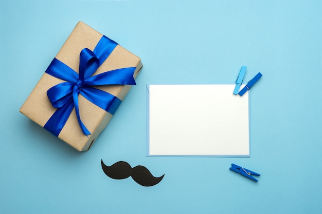 Composition de la fête des pères. Coffret cadeau avec ruban bleu, moustache et carte vierge sur fond bleu.