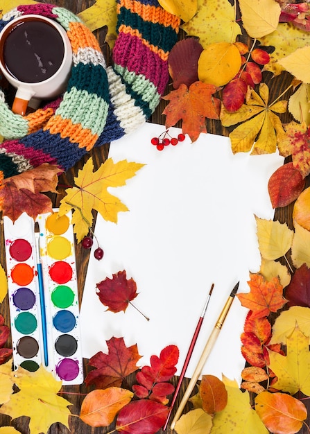 Photo composition avec une feuille de papier blanc peint des pinceaux et des feuilles colorées d'automne