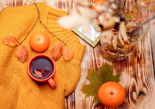 Composition flatlay confortable d'automne. Pull jaune tricoté, tasse fumante de chocolat chaud, mandarines et bouquet de feuilles d'automne. Concept de confort d'automne ou d'hiver.