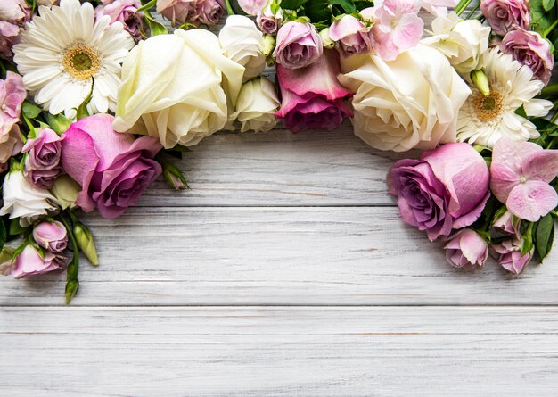Composition de fleurs. Bordure faite de fleurs roses sur fond en bois blanc. Mise à plat, vue de dessus, espace copie