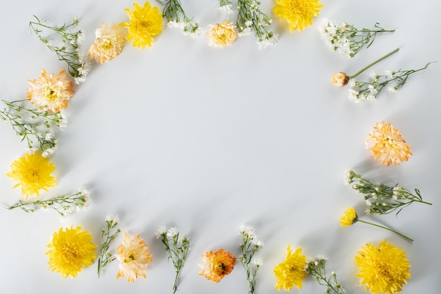 Photo composition de fleurs de chrysanthème et de coupeur motif et cadre faits de diverses fleurs jaunes ou oranges et de feuilles vertes sur fond blanc vue de dessus à plat copie espace printemps été concept