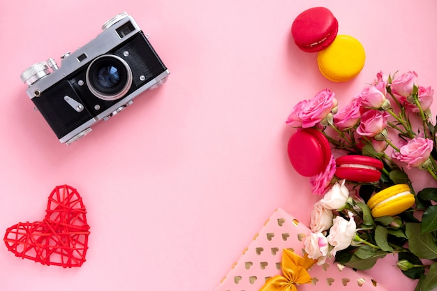 Composition florale avec une couronne de roses roses et appareil photo rétro sur fond rose. Contexte de la Saint-Valentin. Mise à plat, vue de dessus.