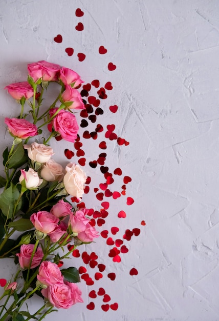 Composition florale avec des roses roses et des coeurs de confettis rouges sur fond gris. Contexte de la Saint-Valentin. Mise à plat, vue de dessus.