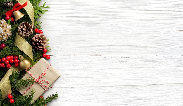 Composition de frontière de Noël faite de boîte-cadeau, branches de sapin, cônes sur fond en bois blanc. Mise à plat, vue de dessus, espace de copie