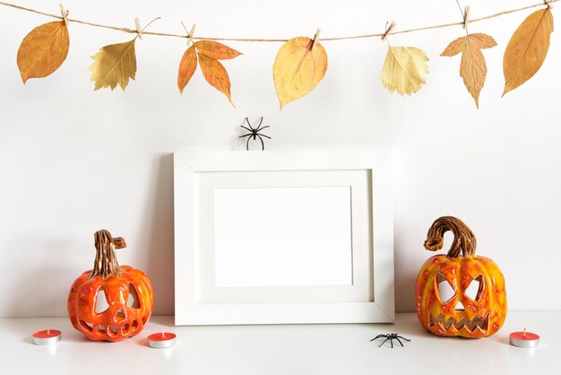 Composition d'Halloween avec guirlande florale de citrouilles en céramique et cadre sur fond de mur de table Modèle de carte de voeux