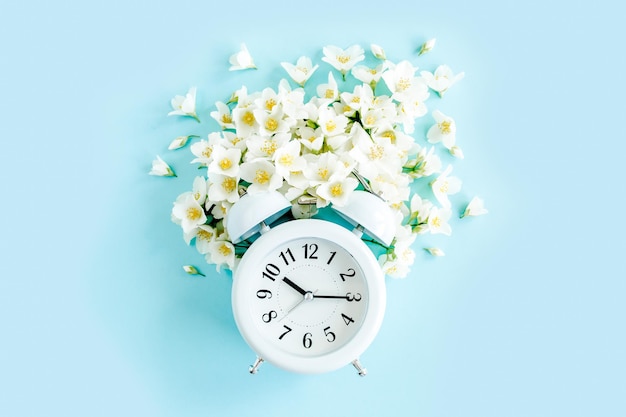 Composition de l'heure d'été de la fleur de jasmin et de l'alarme de l'horloge sur fond bleu vue de dessus à plat