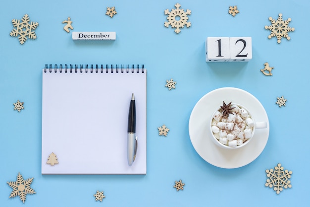 Composition d'hiver. Calendrier en bois 12 décembre Coupe de cacao avec guimauve et anis étoilé, bloc-notes ouvert