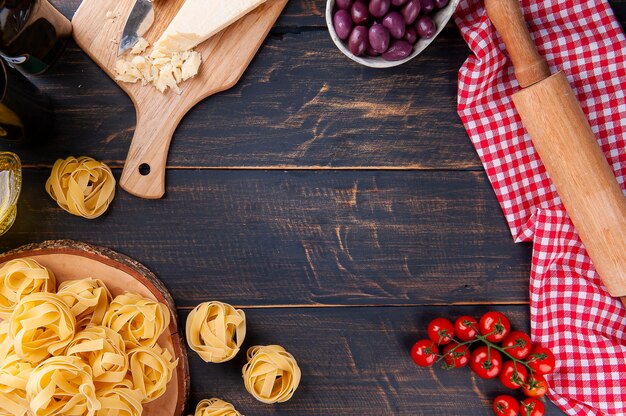 Composition avec des ingrédients pour la préparation de pâtes italiennes. Tomates, parmesan, olives, basilic et pâtes crues. Espace pour le texte