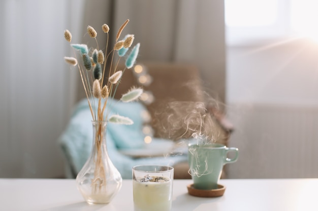 Composition intérieure confortable avec une tasse de café, une bougie et un vase avec des fleurs sur une table basse