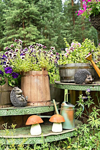 Composition de jardin faite à la main de pots de fleurs en bois avec des figurines en céramique de pétunias de hérissons et d'arrosoirs de champignons