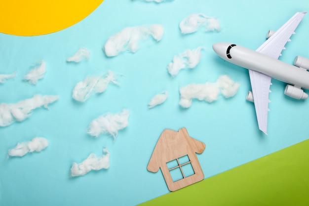 Composition à la main d'une maison sur la pelouse et avion dans un ciel ensoleillé avec des nuages