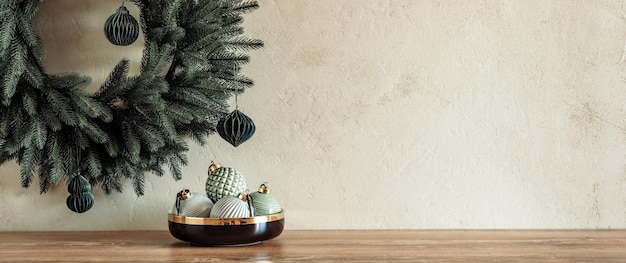 Composition minimale avec des boules de couleur pastel dans un bol sur une table avec une couronne de Noël sur un mur en pierre texturé