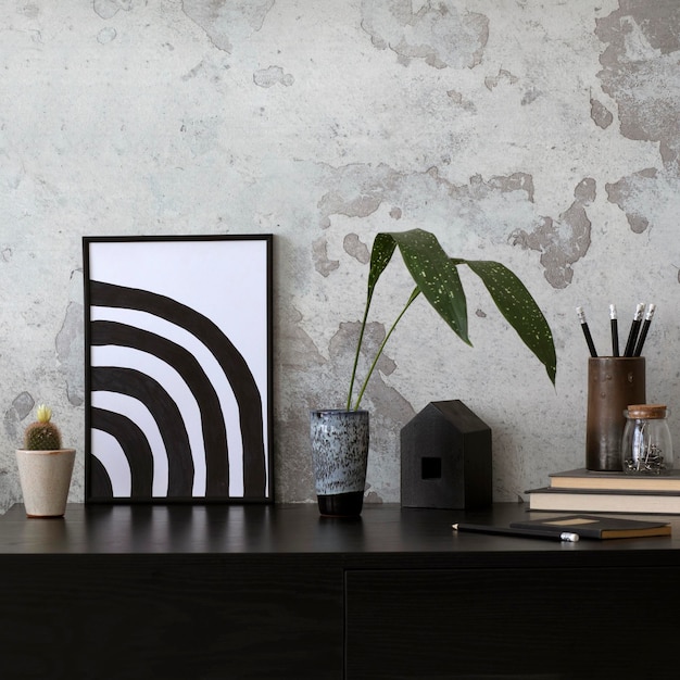 Composition minimaliste de bureau à domicile intérieur en béton avec cadre d'affiche maquette vase de bureau noir avec feuilles livres cactus et accessoires de bureau Mur de béton gris Modèle de décoration