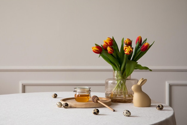 Composition minimaliste de l'intérieur de la salle à manger de Pâques avec copie espace table ronde vase avec tulipes lapin de Pâques sculpture miel en pot mur beige et accessoires personnels Modèle de décoration