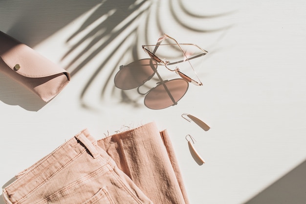 Composition de mode avec des vêtements et accessoires pour femmes sur blanc. Boucles d'oreilles, lunettes de soleil, jupe-culotte en jean rose sur blanc