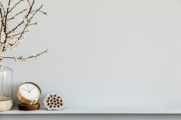 Composition moderne sur l'étagère avec fleur séchée dans un vase design, horloge en or, accessoires et décoration. Mur gris. Espace de copie.