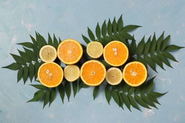 Composition de moitiés de citrons et d'oranges avec des feuilles vertes sur une surface bleu clair, mise à plat