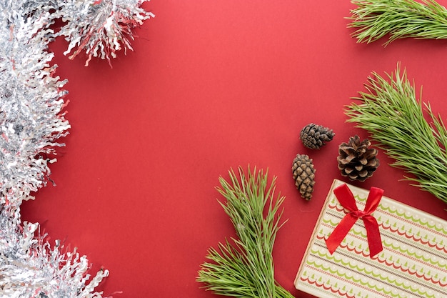Composition de Noël. Une boîte avec un cadeau et des branches d'épinette sur fond rouge. Cônes d'épinette et décorations de Noël. Mise à plat, vue de dessus, espace pour le texte