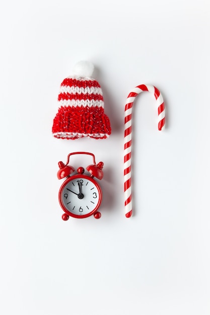 Composition de Noël, bonbons de canne, petite horloge analogique, chapeau rayé sur mur blanc. Style minimal. Vue de dessus. Concept de vacances et de fête.