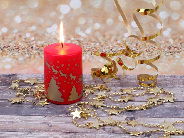 Composition de Noël de la bougie brûlante de Noël rouge, des étoiles d'or et de la guirlande sur une surface en bois