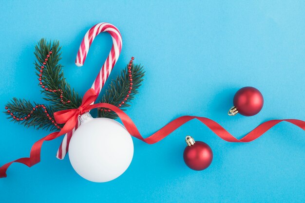 Composition de Noël avec boule blanche, branches d'épinette et canne au caramel sur la surface bleue. Vue de dessus. Copiez l'espace.