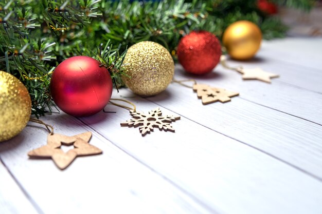 Composition de Noël avec des branches de sapin, des ballons dorés et rouges, des jouets en bois sur un fond en bois blanc.