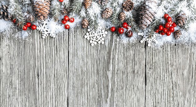 Composition de Noël. Cadre fait de branches de sapin, de cônes et de baies de Noël rouges recouvertes de neige sur fond de bois ancien. Vue de dessus, mise à plat, espace de copie