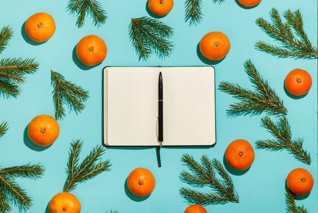 Composition de Noël. Cadre de Noël avec des mandarines, du sapin et un cahier ouvert sur une table verte. Mise à plat, vue de dessus