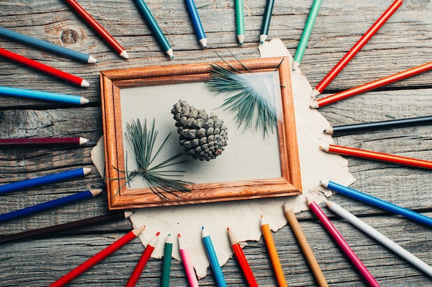 Composition de Noël, cadre photo sur table en bois, branches d'arbres et cônes éparpillés autour de différentes couleurs