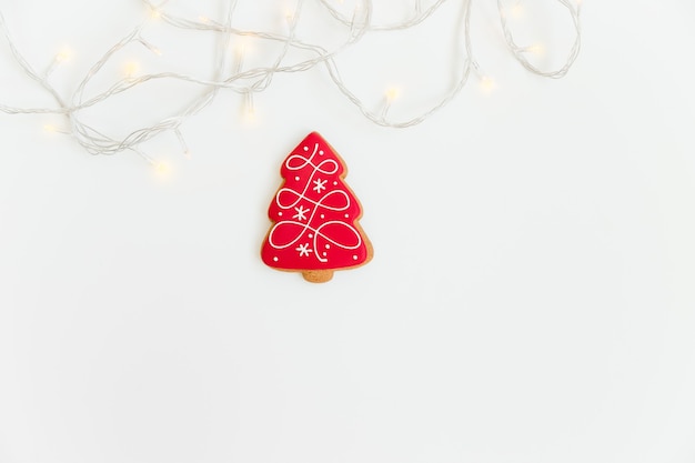 Composition de Noël créative avec biscuit de pain d'épice rouge et lumière de Noël. Mise à plat. Sapin de Noël. Copiez l'espace.