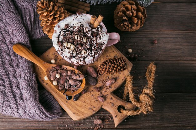 Composition de Noël ou du nouvel an avec une boisson au chocolat chaud ou au cacao avec de la crème fouettée servie avec du chocolat haché et des fèves de cacao sur une plaque en bois rustique. Vue de dessus