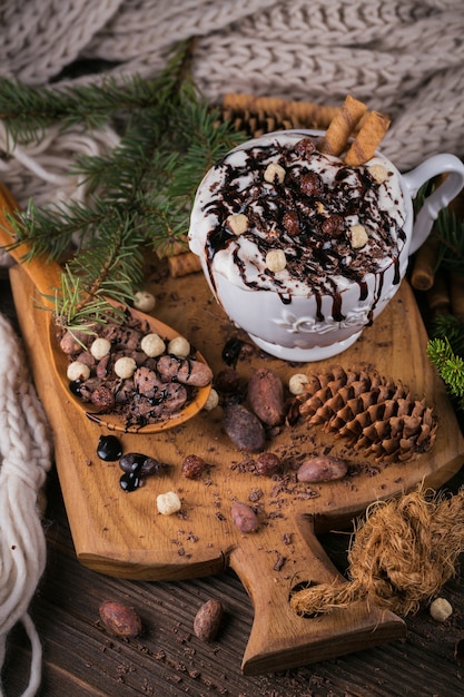 Composition de Noël ou du nouvel an avec une boisson au chocolat chaud ou au cacao avec de la crème fouettée servie avec du chocolat haché et des fèves de cacao sur une plaque en bois rustique.